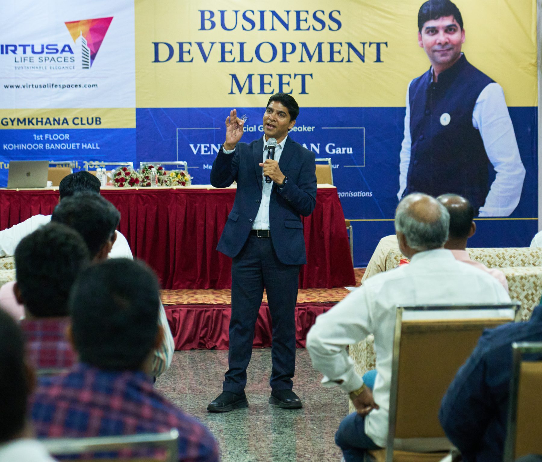Speaking to a seated audience at a business development meet